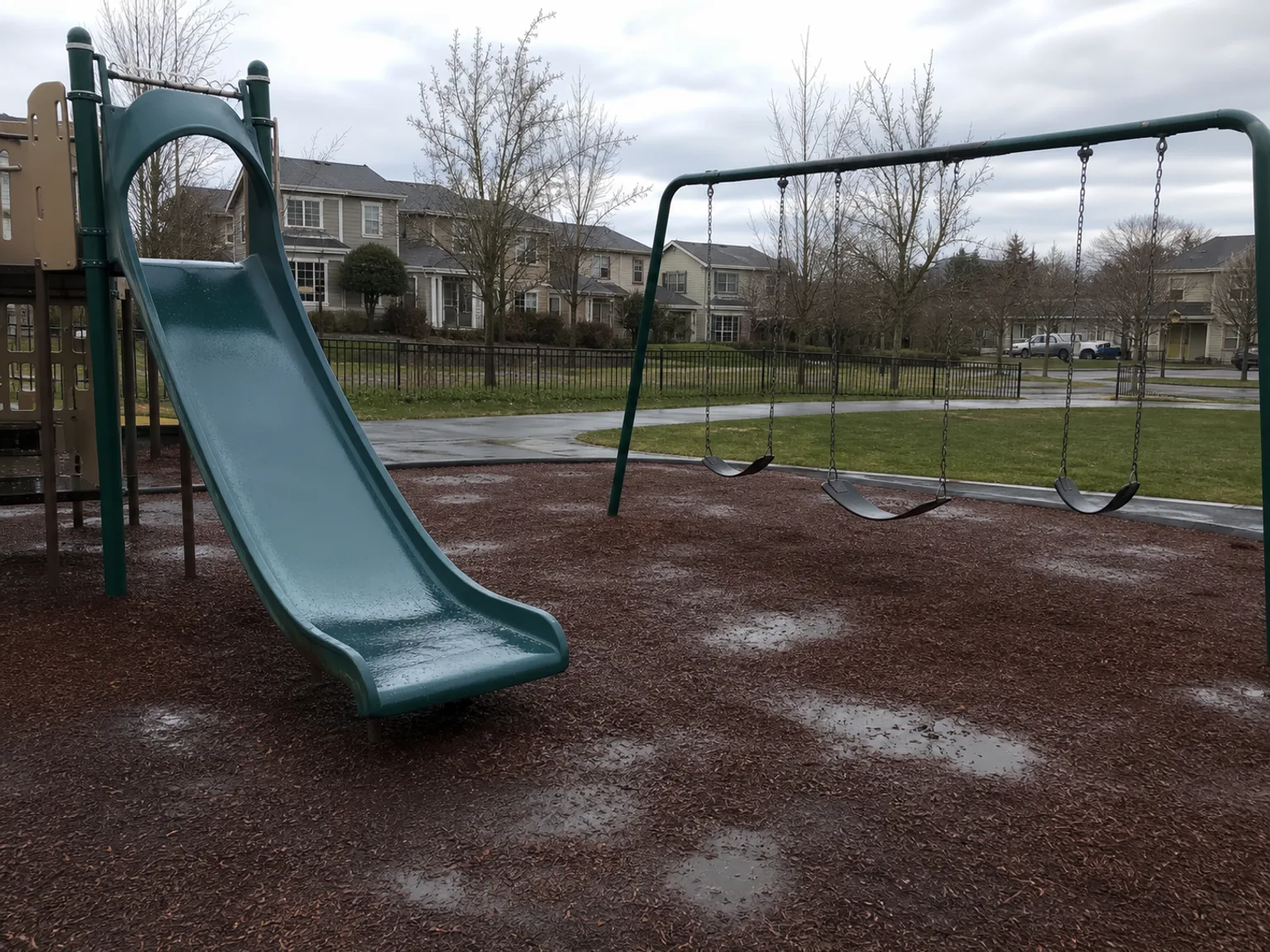 Um parque infantil vazio com escorrega e baloicos aparece sob um ceu nublado.
