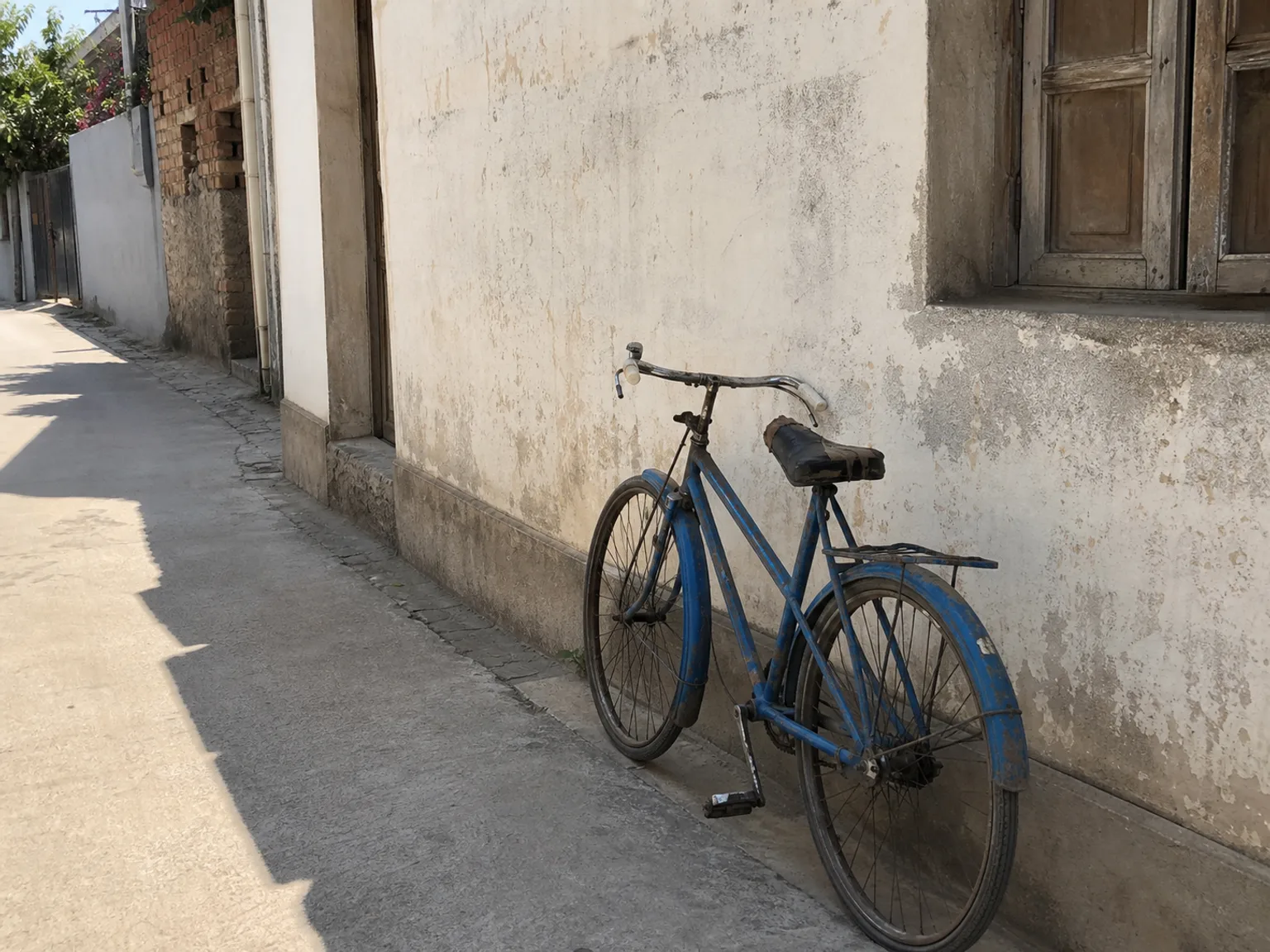 Uma bicicleta azul apoia-se numa parede iluminada numa rua estreita.