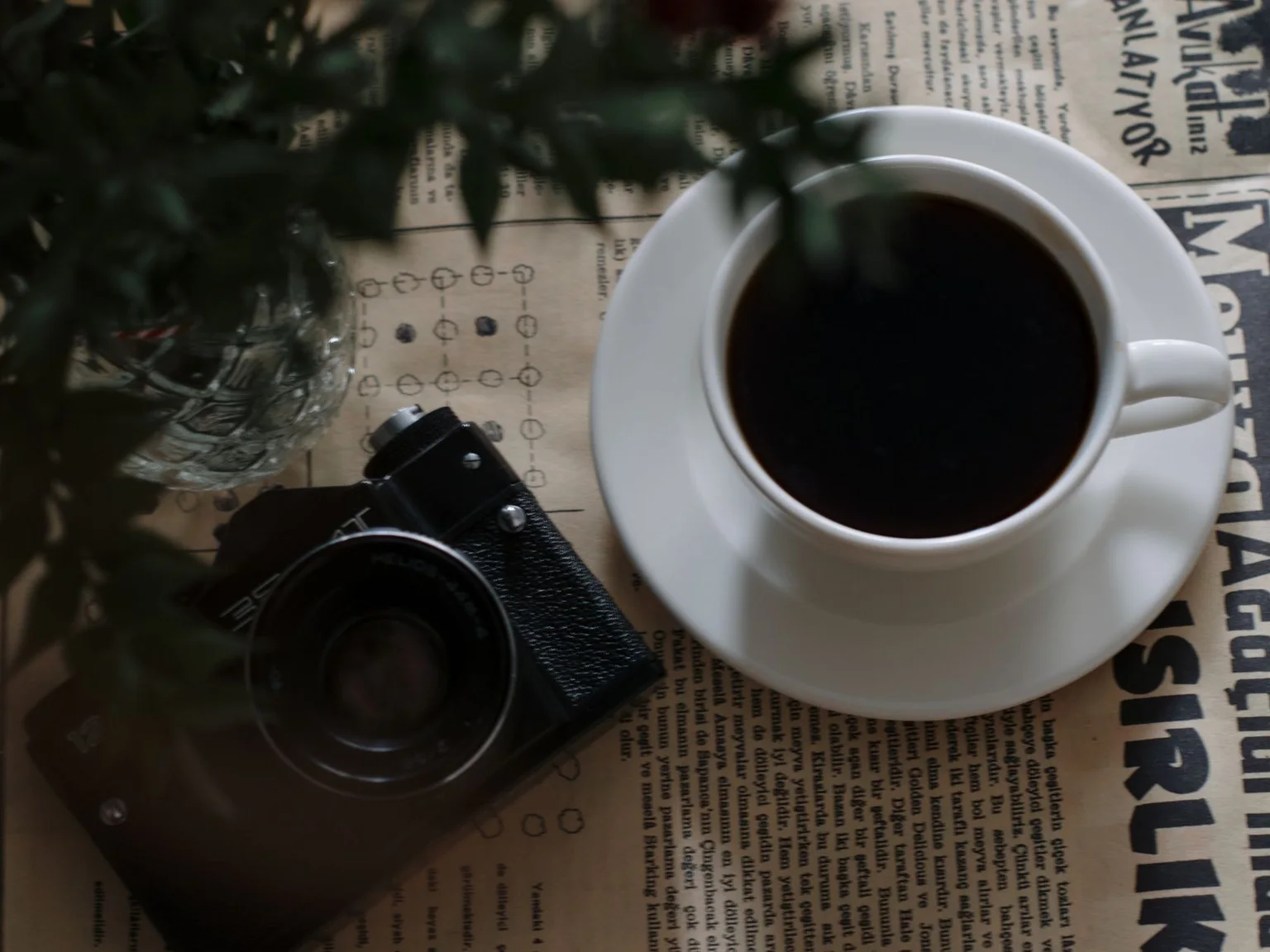 Uma chavena de cafe esta junto a uma camara compacta sobre papel impresso.