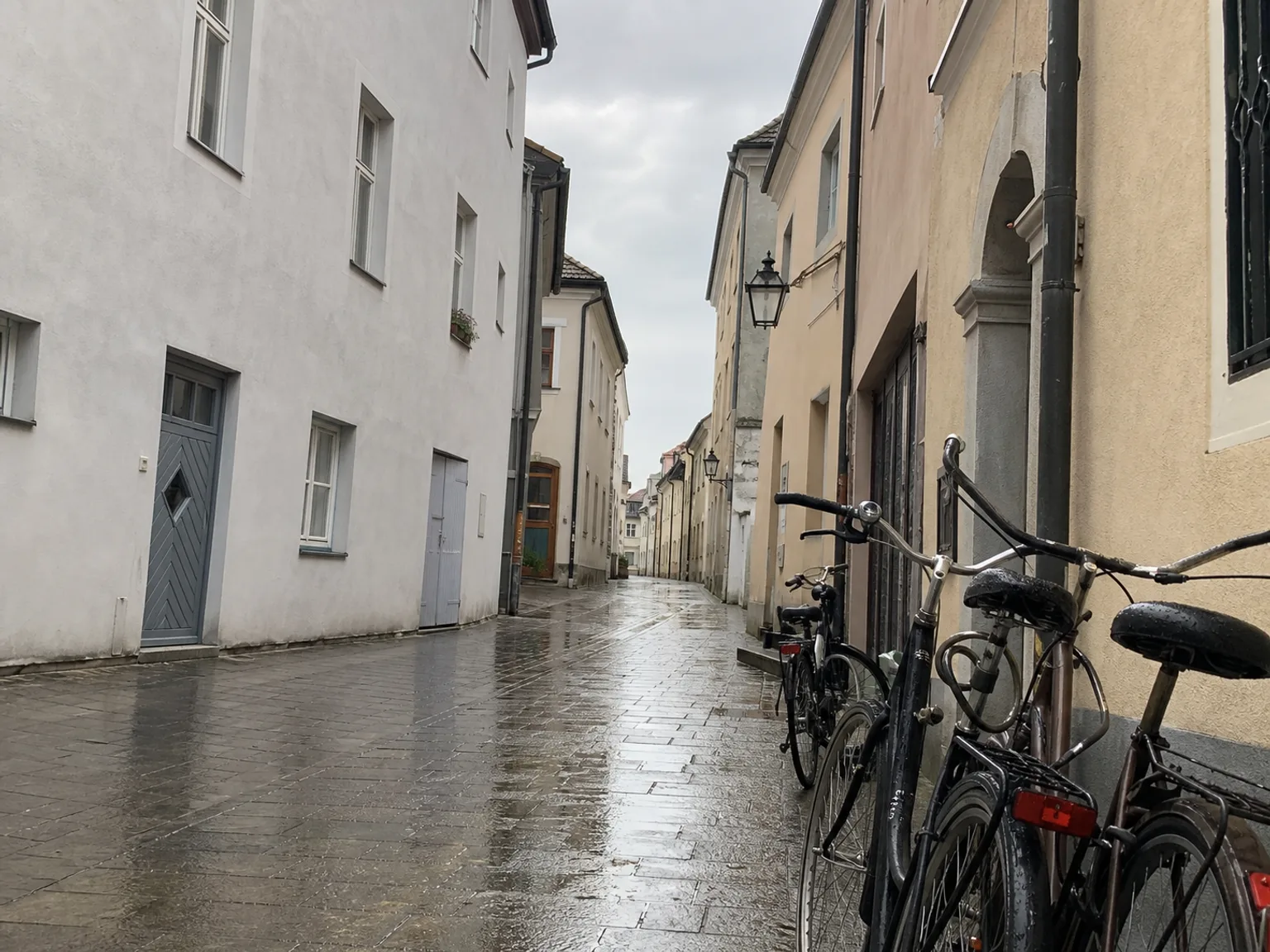 Uma rua estreita brilha depois da chuva entre fachadas antigas.