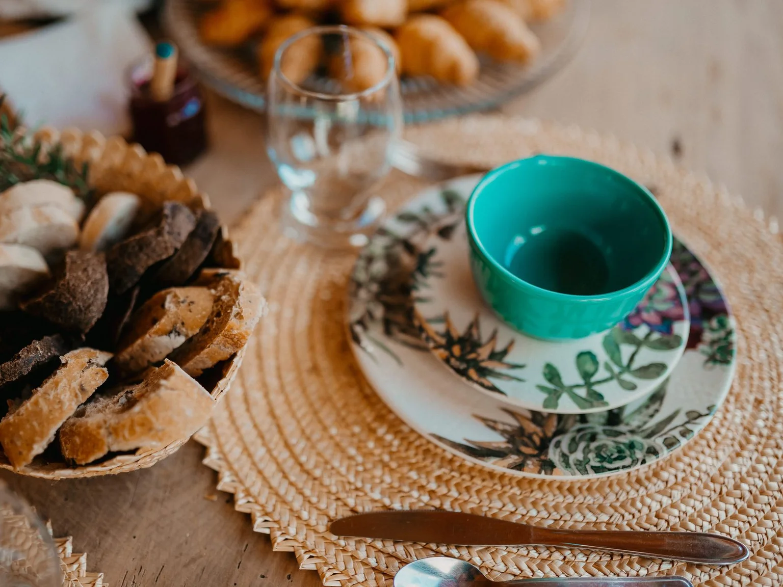 Uma mesa de pequeno-almoco inclui uma chavena turquesa, pao e pinhas decorativas.