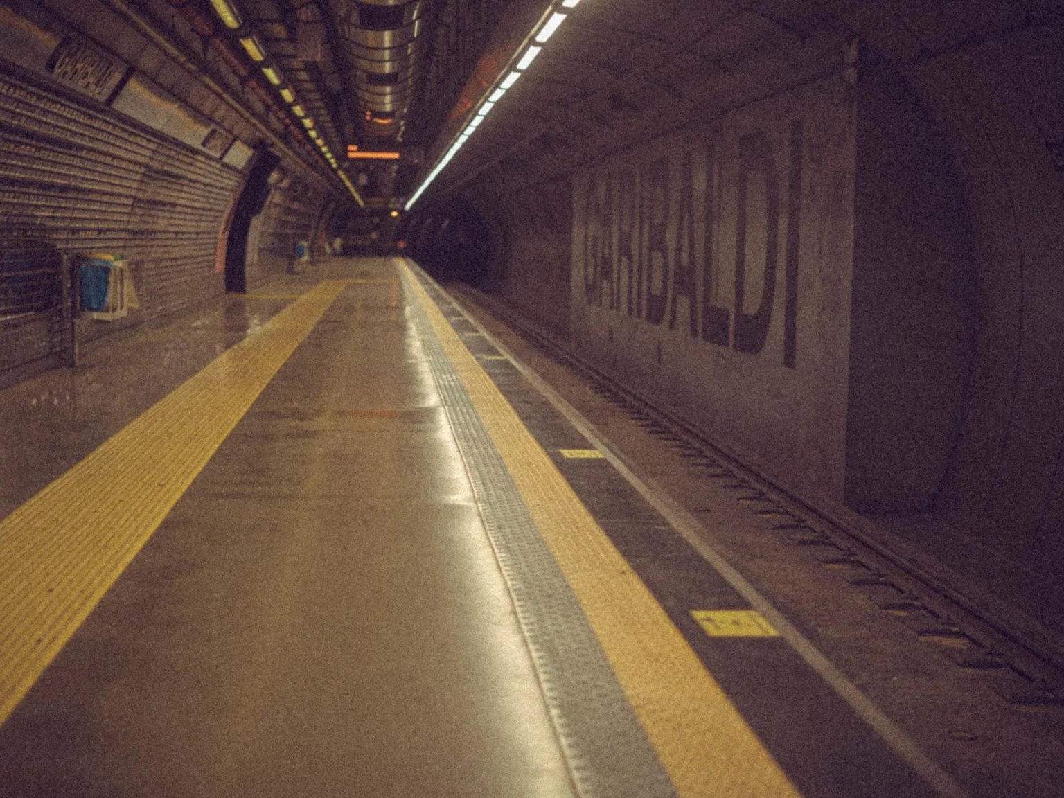 Uma plataforma de metro vazia prolonga-se para um tunel com linhas amarelas de seguranca.