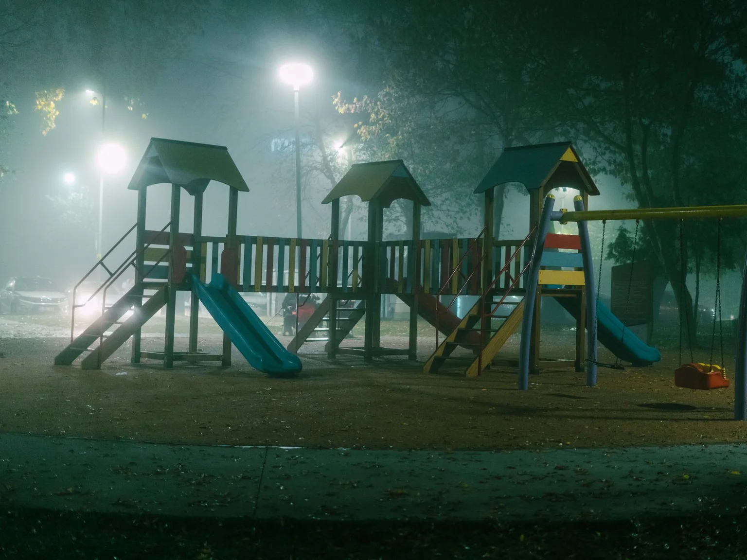 Um parque infantil esta iluminado por luzes intensas numa noite com nevoeiro.