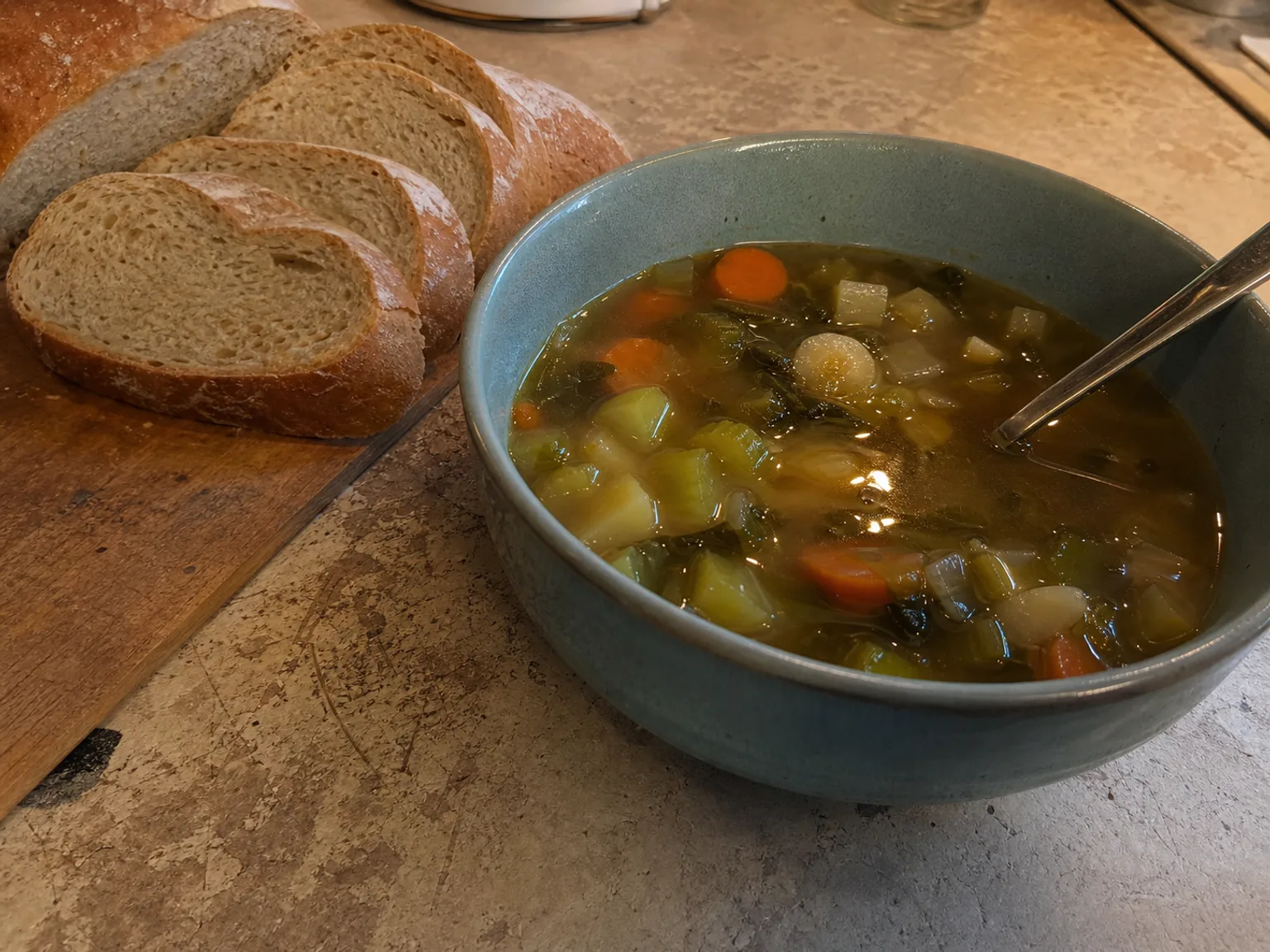 Uma tigela de sopa de legumes esta junto a fatias de pao.