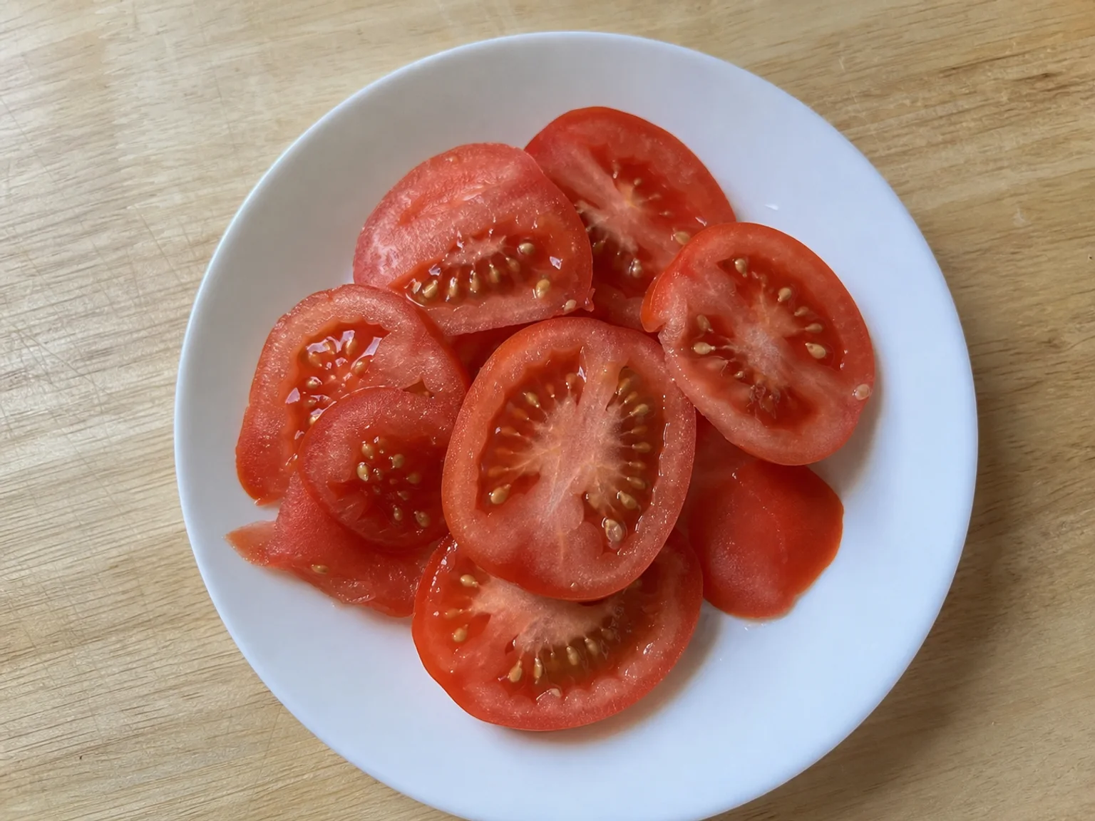 Rodelas de tomate estao colocadas num prato branco sobre uma mesa de madeira.