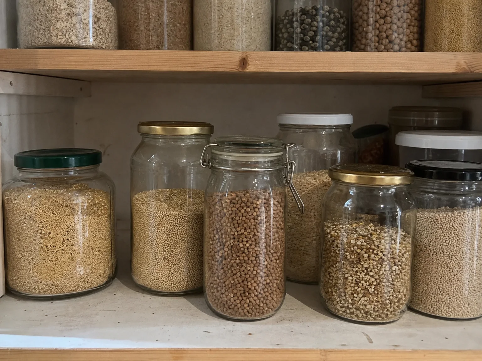 Frascos de vidro com cereais e sementes estao alinhados numa despensa.