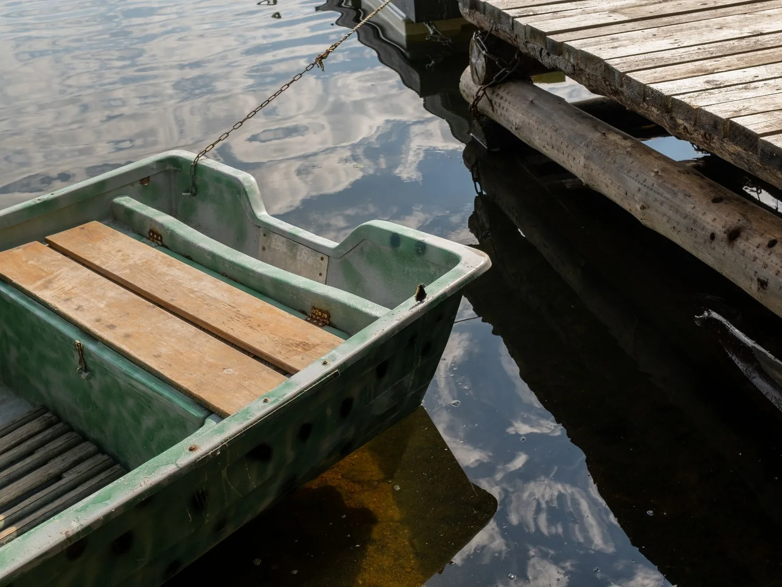 Un bote verde está amarrado junto a un muelle de madera sobre agua quieta.