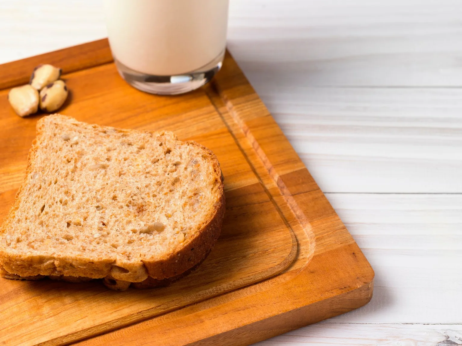 Una rebanada de pan y un vaso de leche reposan sobre una tabla de madera.