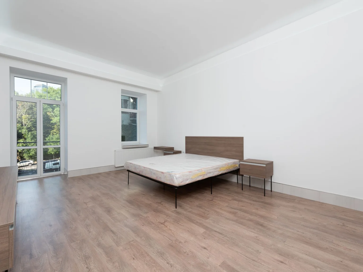 Um quarto minimalista tem uma cama baixa, paredes claras e janelas grandes.