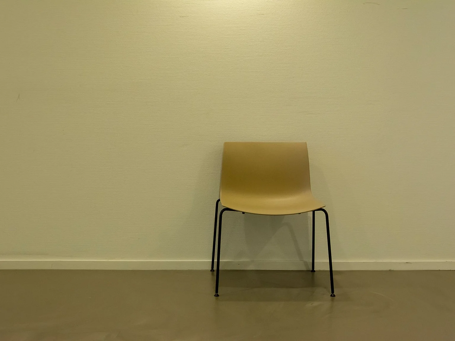 Uma cadeira amarela solitaria esta diante de uma parede clara e lisa.
