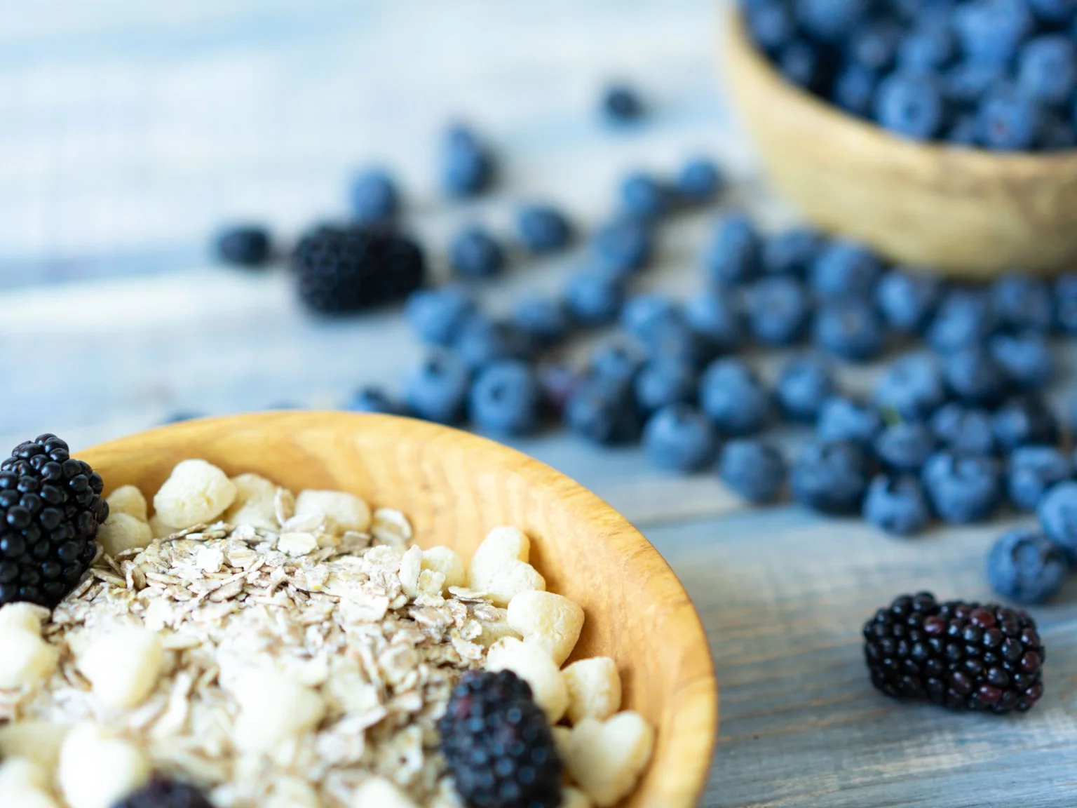Uma taca de aveia esta rodeada de frutos silvestres escuros e frescos.