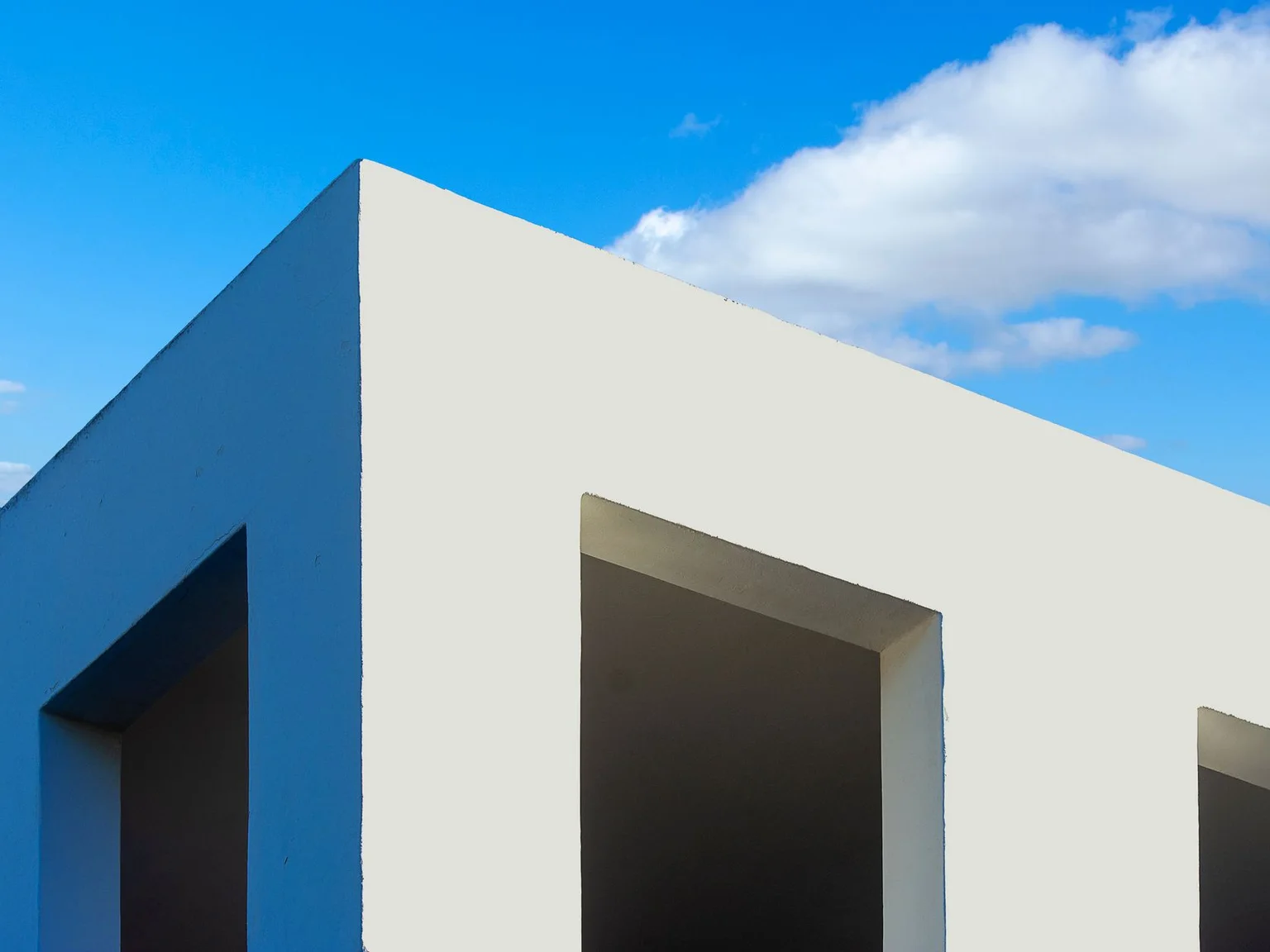 A esquina de um edificio branco moderno destaca-se contra um ceu azul intenso.