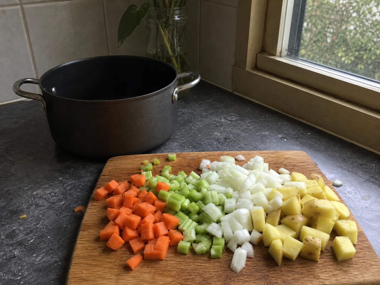 Legumes cortados estao sobre uma tabua junto a uma panela.