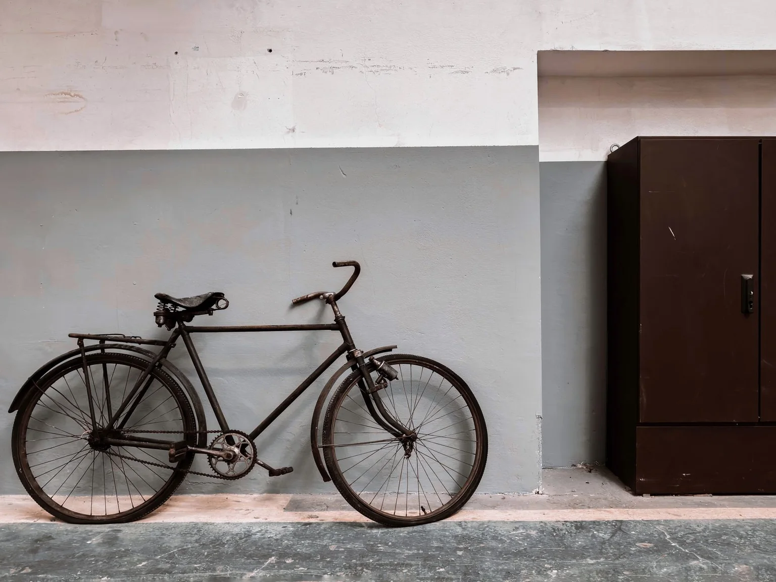 Uma bicicleta classica esta junto a uma parede lisa e uma porta escura.
