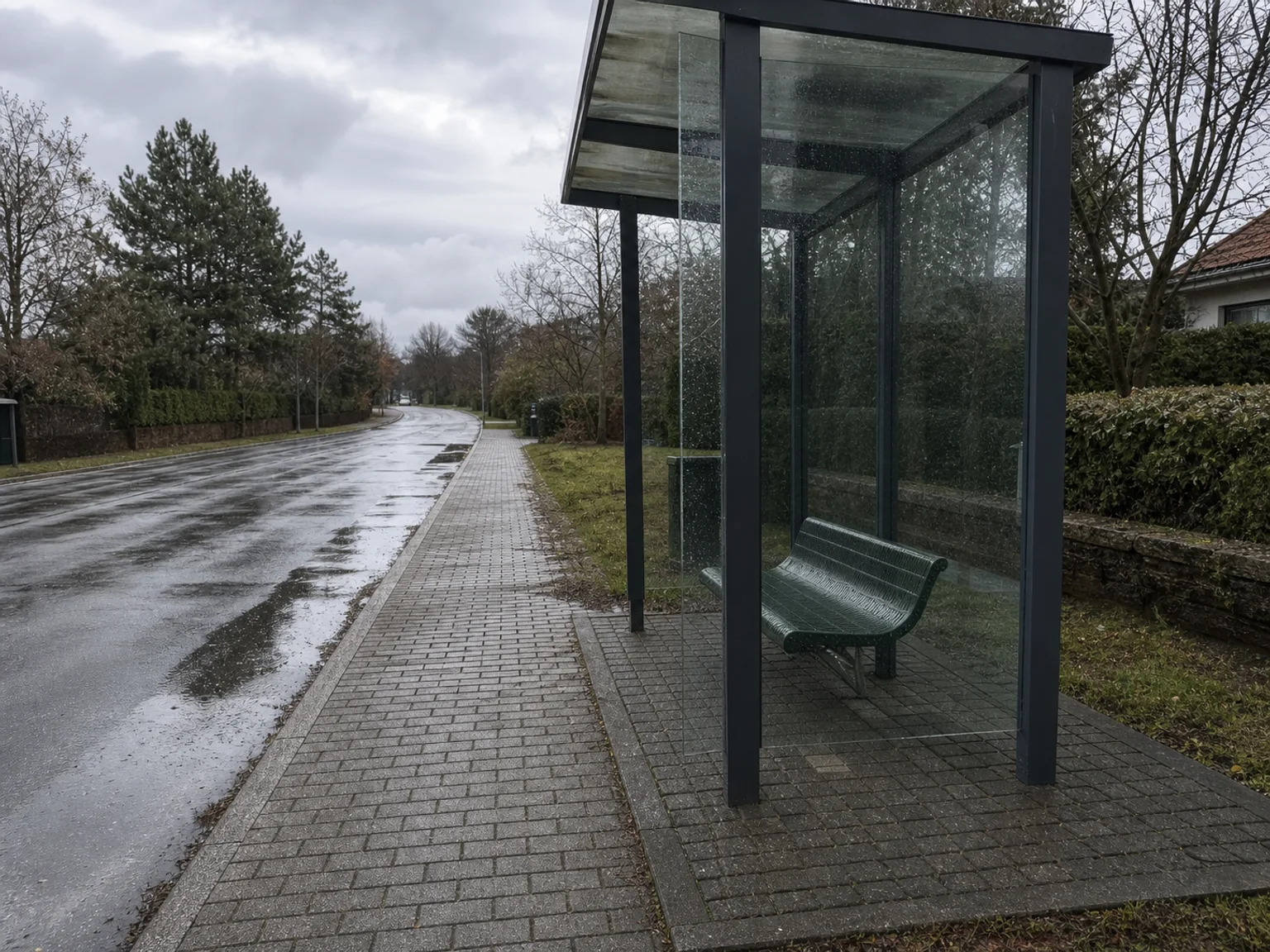Uma paragem de autocarro envidracada esta junto a uma estrada molhada depois da chuva.