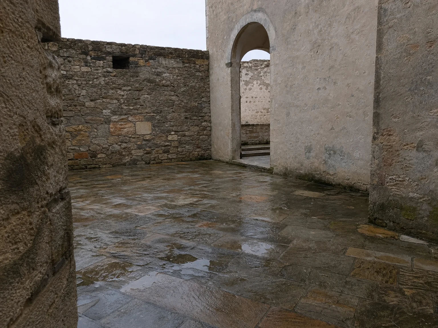 Um patio de pedra molhada fica entre muros antigos e arcos.