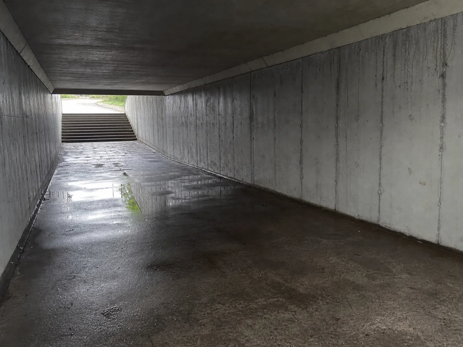 Uma passagem subterranea de betao conduz para a luz e o pavimento molhado.