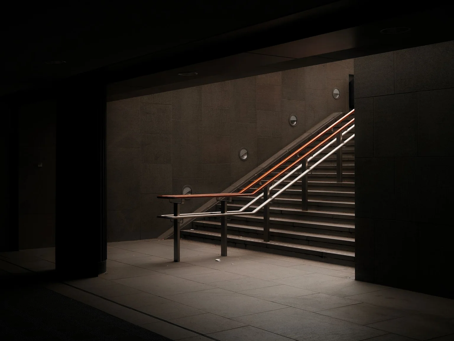 Escadas subterraneas escuras estao iluminadas por faixas estreitas de luz.