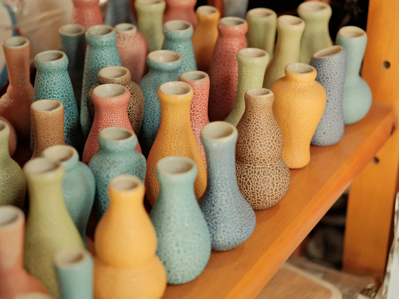 Filas de vasos de ceramica coloridos enchem uma prateleira.